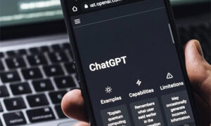 Mobile phone held in hand displaying the ChatGPT app with the words ‘Examples’, ‘Capabilities’, and ‘Limitations’ visible on screen.